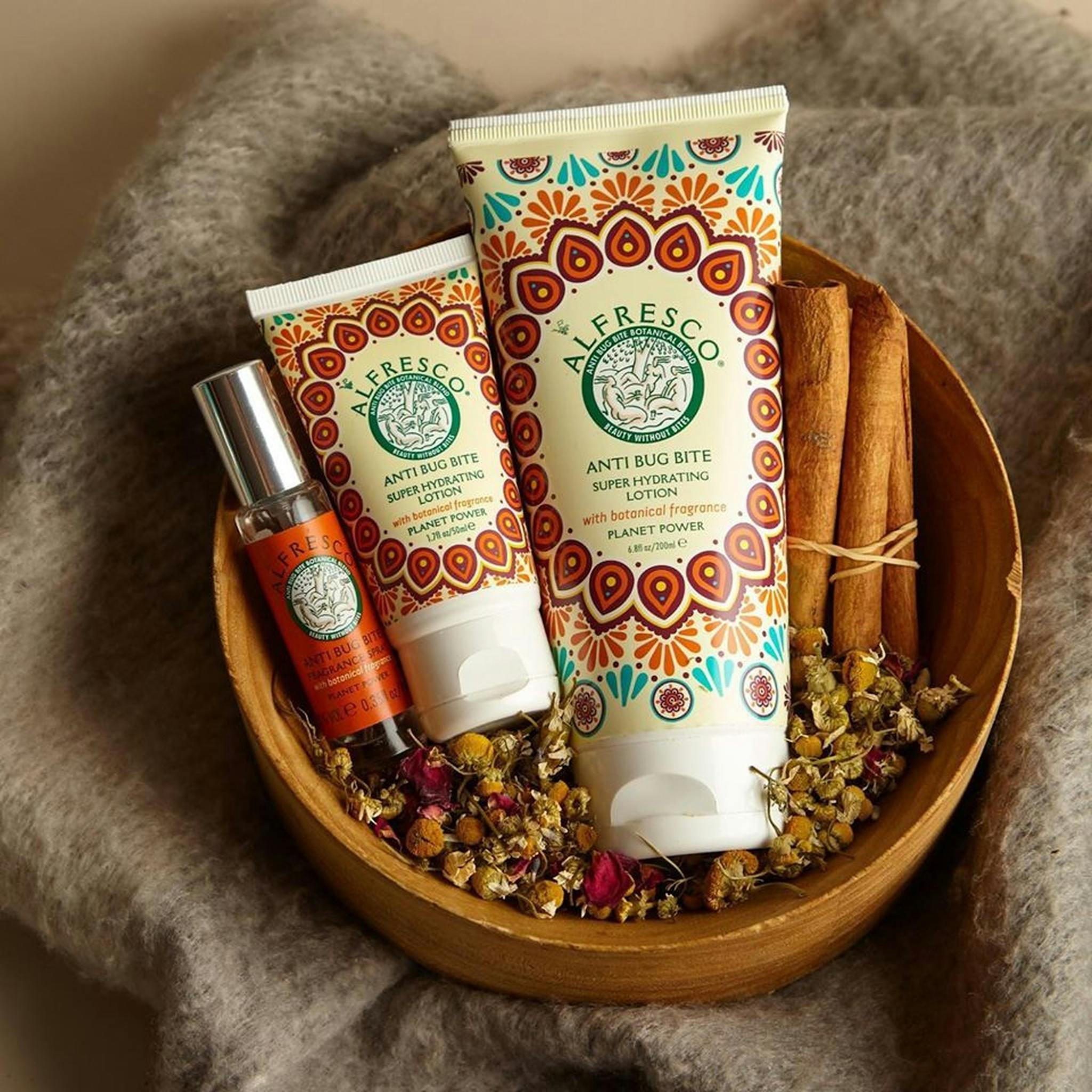 A set of anti-bug bite cosmetic products in a wooden bowl accompanied by cinnamon sticks and dried flowers.