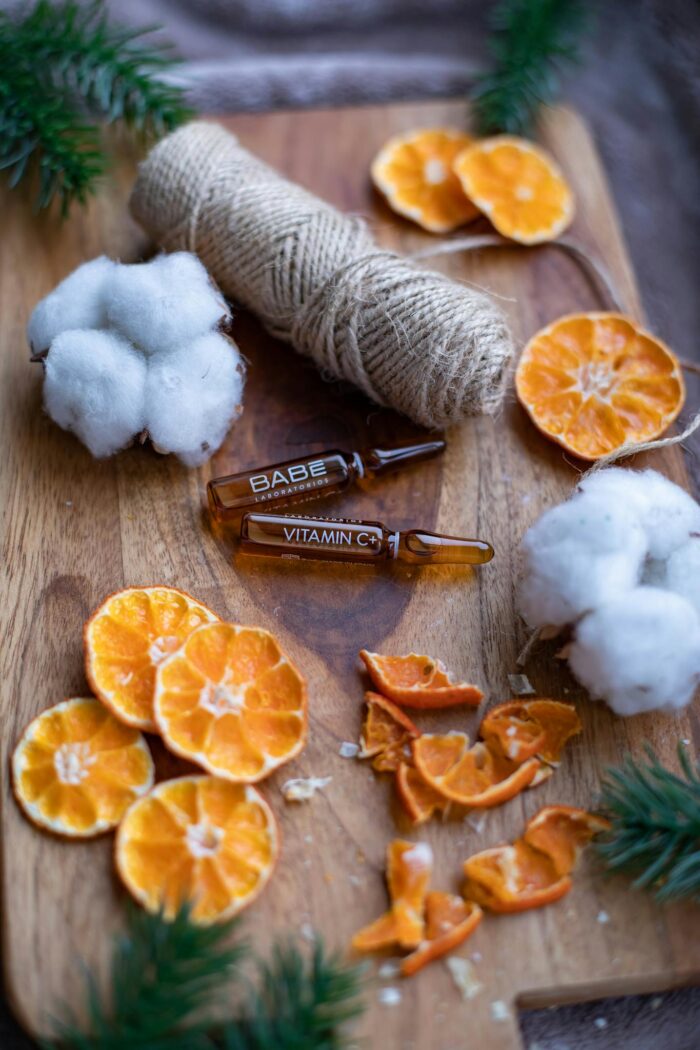 Aesthetic vertical shot featuring vitamin C serum, cotton, and dried oranges on a wooden board.