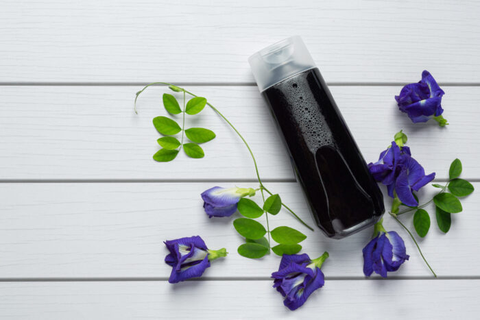 Shampoo bottle of butterfly pea flower put on white wooden backg