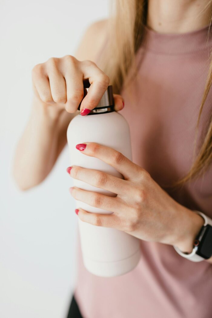 Close-up of a woman opening a lotion bottle showcasing her stylish manicure and smart watch.