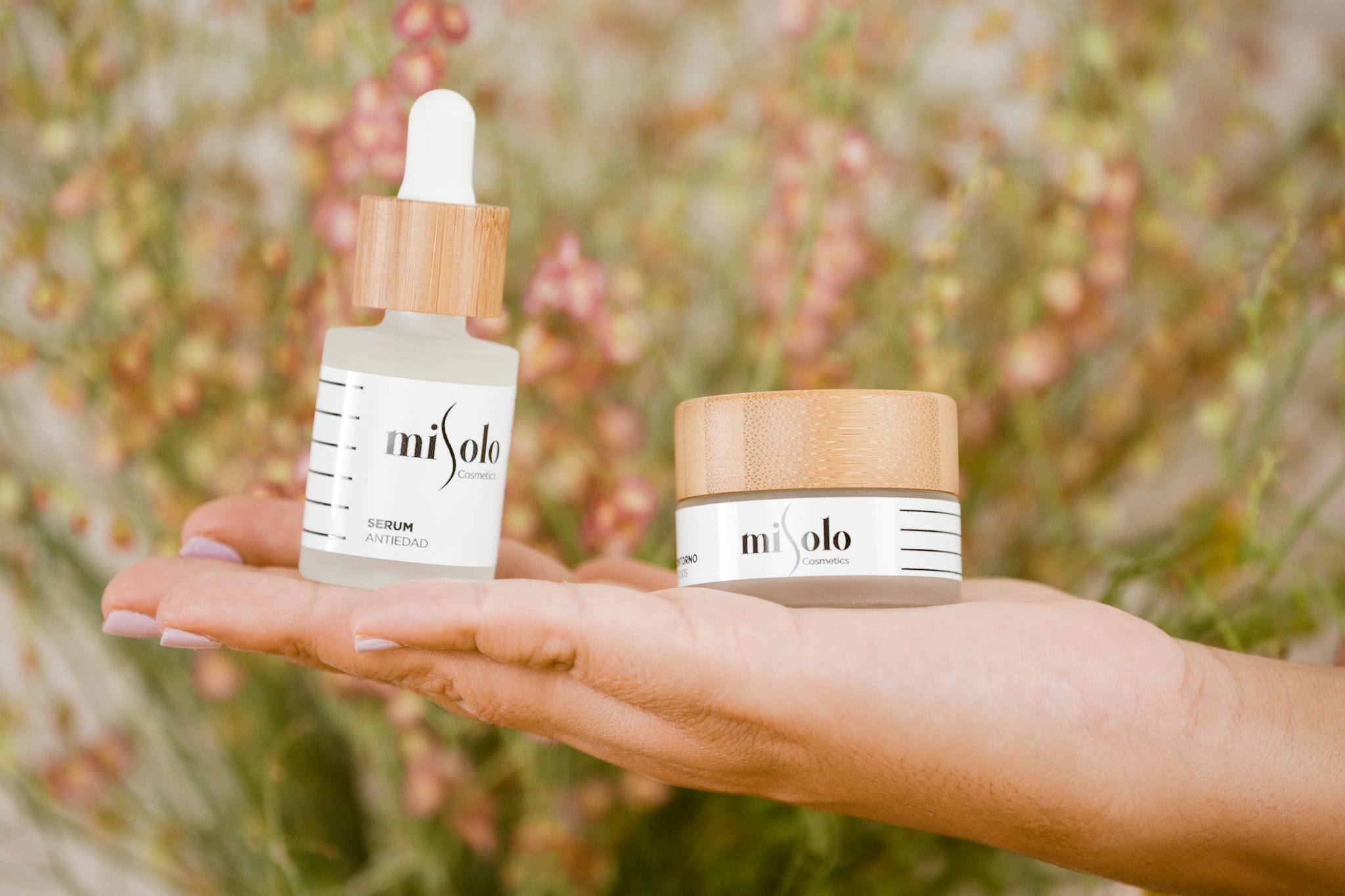 Close-up of hands holding natural cosmetic products outdoors with a floral background.