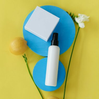 Creative flat lay of beauty products with lemons and flowers on a colorful yellow and blue background.