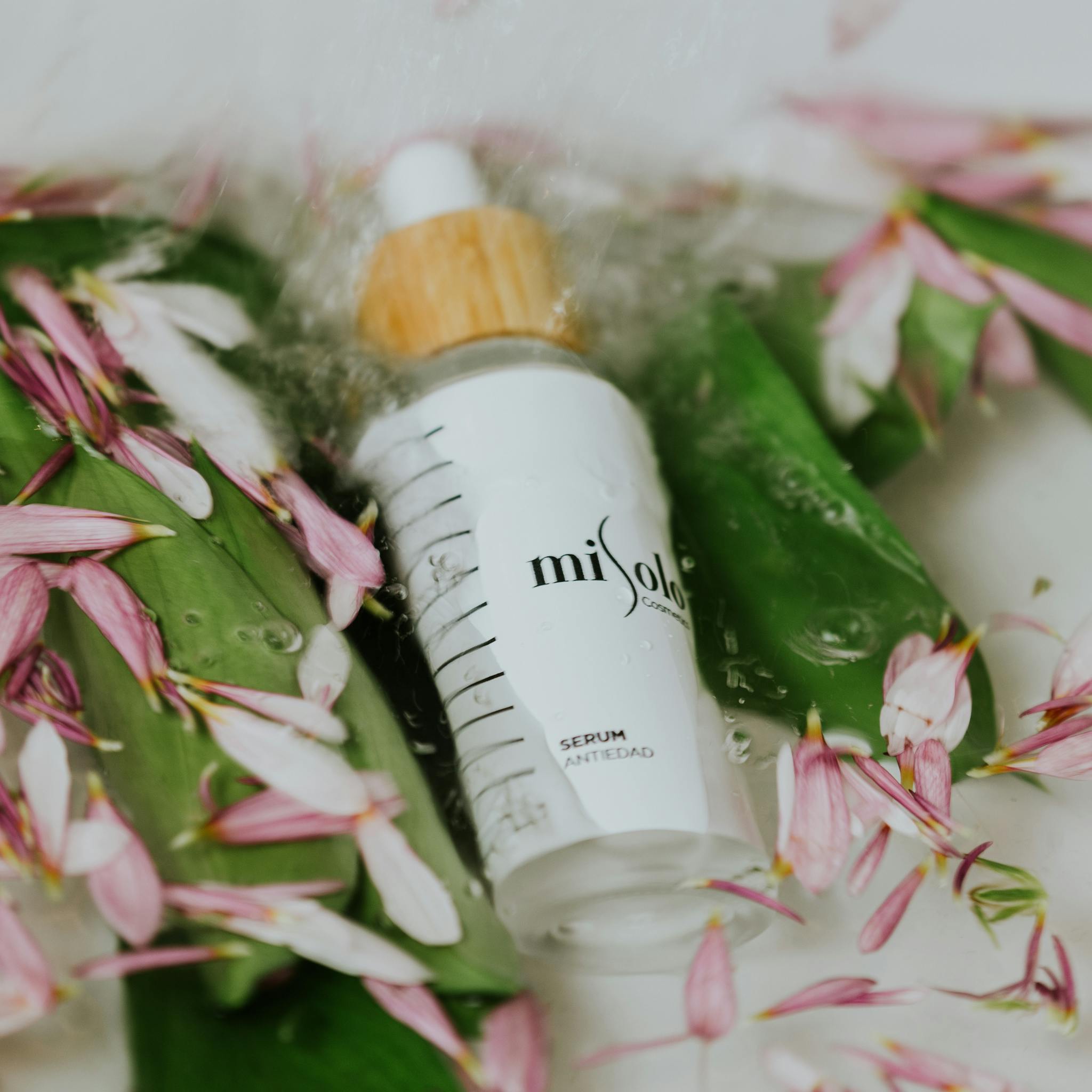 Elegant skincare serum bottle surrounded by pink petals and green leaves, highlighting luxury beauty.