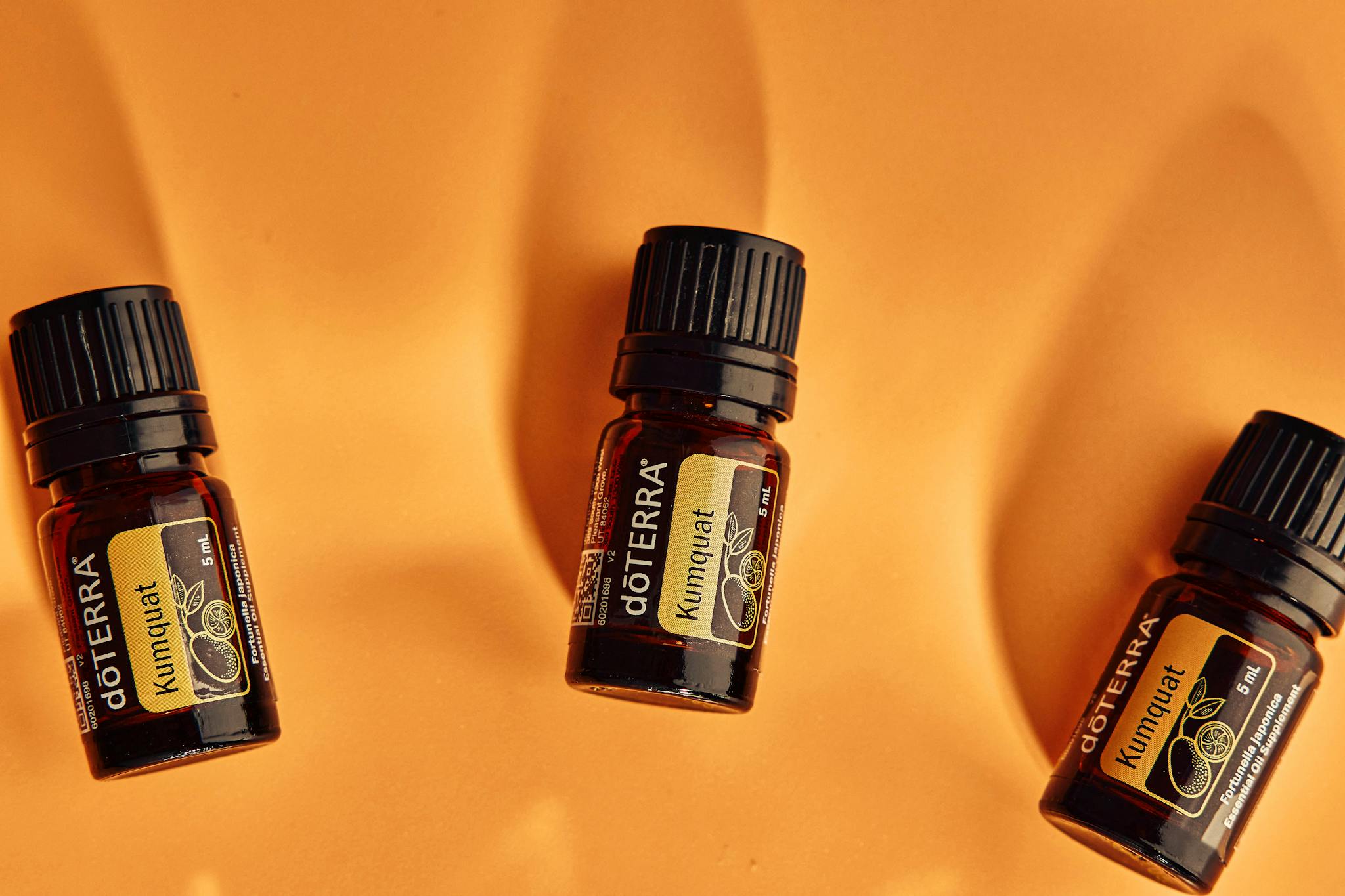 Flat lay of dōTERRA kumquat essential oil bottles on an orange background.