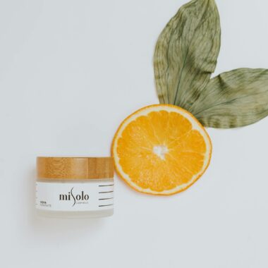 Overhead view of skincare cream with natural ingredients like orange and leaves for luxurious beauty.
